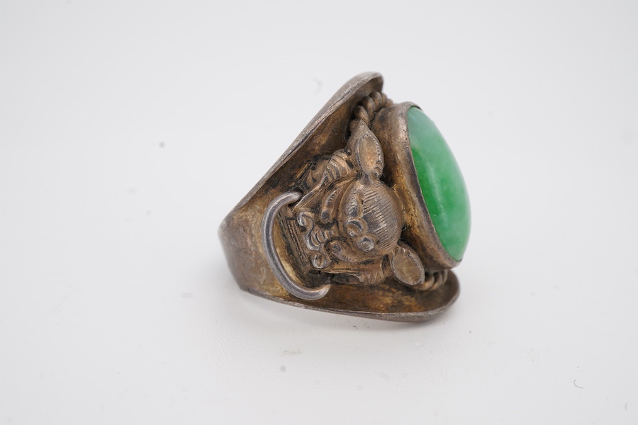 A 20th century Chinese white metal and single stone cabochon jade set ring, the shoulders decorated with lion-dogs, size L.